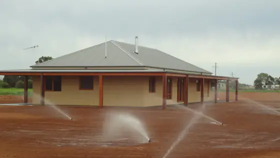 Pop-up sprinklers watering bare soil in front of a new brick home