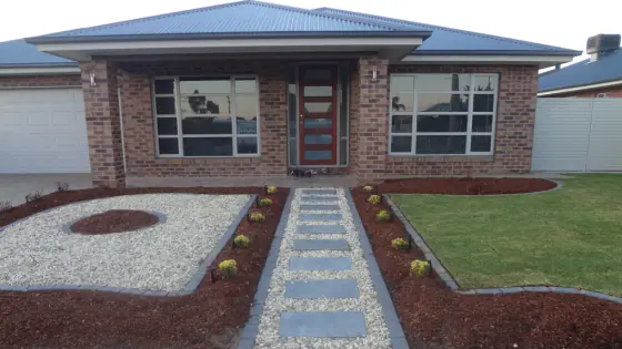 Front yard with a paver path through white pebbles and new lawn leading to a brick home