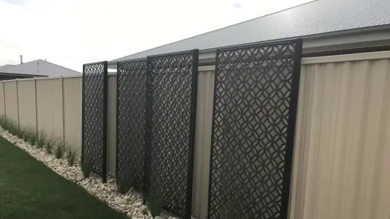 Black decorative lattice screens along a side fence above a pebble border and lawn