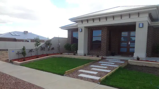 Front garden with a stepping stone path, red pebbles and new lawn
