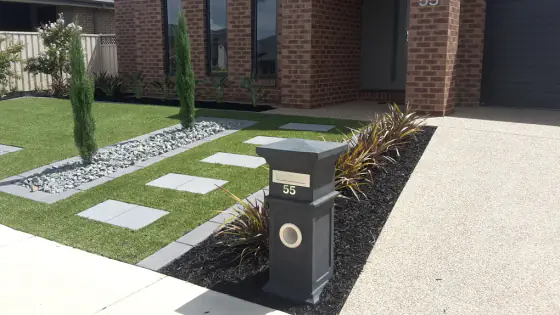 Front garden with square pavers, white pebbles, dark mulch and a letterbox