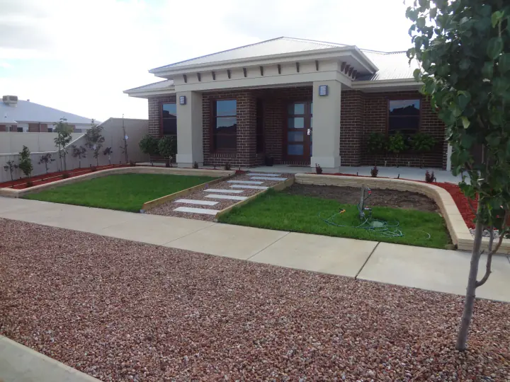 Newly laid front lawn being watered, with a sandstone wall and stepping stone path
