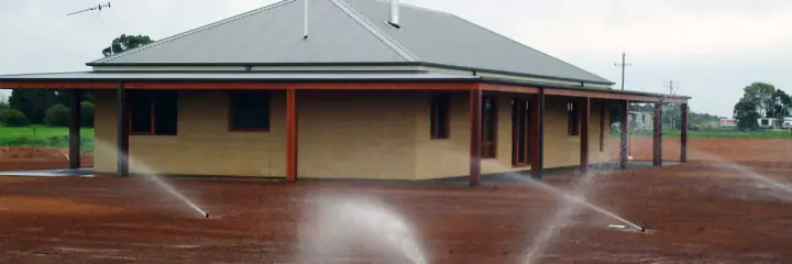 Pop-up sprinklers spraying water beside a new house