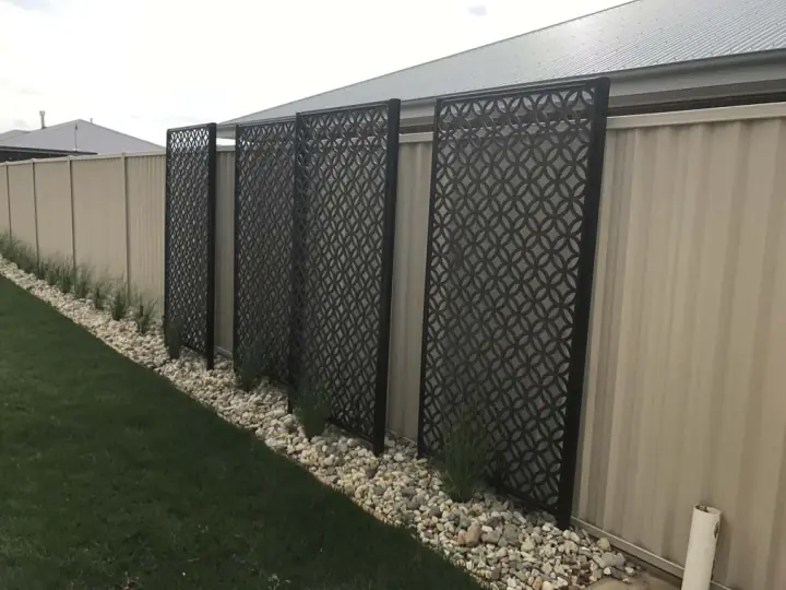 Black decorative lattice screens along a side fence above a pebble border and lawn