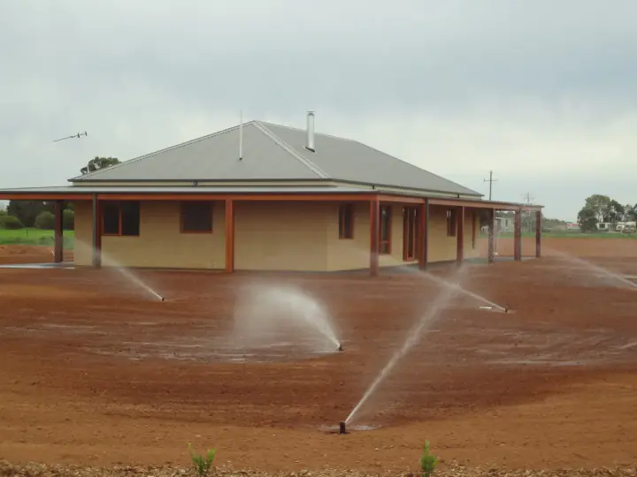 Pop-up sprinklers watering bare soil in front of a new brick home